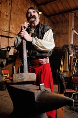 portrait of a blacksmith with a beautiful thick mustache with a huge hammer in the hands on the background of the forge.