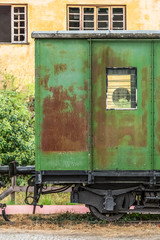 Fototapeta na wymiar View of a abandoned and older rustic train wagon, yellow building as background