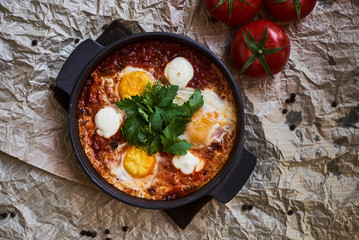 Shakshuka with eggs, tomatoes and parsley in a frying pan, close-up