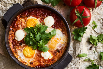Shakshuka with eggs, tomatoes and parsley in a frying pan, close-up