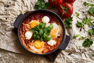 Shakshuka with eggs, tomatoes and parsley in a frying pan, close-up