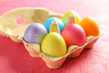 Fototapeta na wymiar Decorative eggs in cardboard box on color background. Closeup