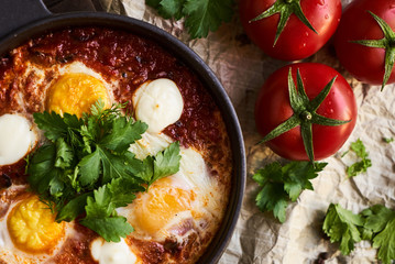 Shakshuka with eggs, tomatoes and parsley in a frying pan, close-up