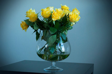 Yellow roses in a glass vase on a black wooden table