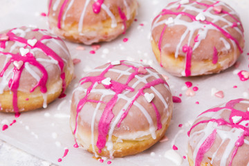 Traditional Polish donuts with pink frosting and heart sprinkles on light background. Tasty doughnuts with jam.