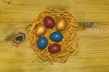 Painted Easter eggs in a straw on wooden table.Toned photo.