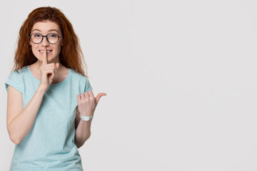 Red-haired girl holding finger on lips to keep it quiet