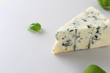 a piece of blue cheese on a light gray basil background