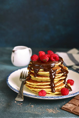 Stack of homemade pancakes with chocolate topping and fresh raspberry.