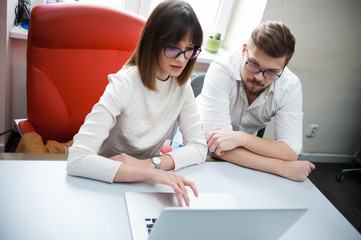 Two young coworkers dressed casual using laptop in white interior