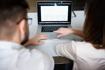 Two young coworkers dressed casual using laptop in white interior