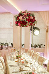 A table in a restaurant during a wedding celebration, decorated with a bouquet of red flowers on a stand.