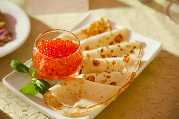 Pancakes with fresh red caviar on a white plate.