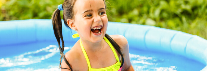A little girl is played by a water pump in an inflatable pool in the garden near the house