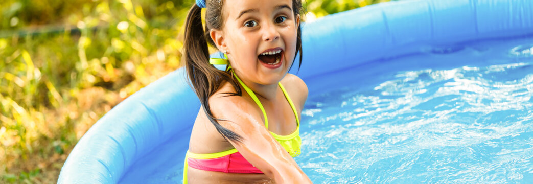 Little girl in an inflatable pool in the garden near the house