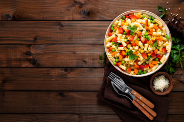Italian pasta salad with fusilli, corn, boiled carrot, fresh green peas and sweet pepper on wooden rustic background. Top view