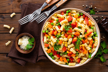 Italian pasta salad with fusilli, corn, boiled carrot, fresh green peas and sweet pepper on wooden rustic background. Top view