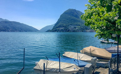 Ufer des Luganersee (Lake Lugano) im Tessin, Schweiz. Blick auf die Berge und blauer Himmel. Bootsteg am Ufer. 