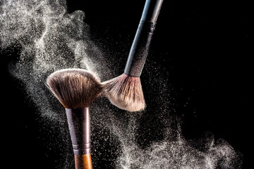 Make up cosmetic brushes with powder blush explosion on black background. Skin care or fashion...