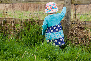View of little toddler girl from behind playing in grass beside a fence