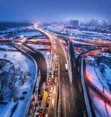 Aerial view of the road in modern city at night in fog. Top view of traffic in highway. Winter cityscape with elevated road, cars, buildings, illumination.  Interchange overpass in Europe. Expressway