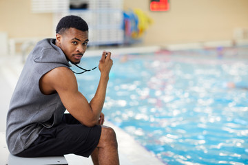 Side view portrait of handsome African-American fitness coach looking at camera in swimming pool,...