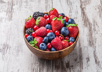 Berries fresh mix close-up arrangement in old rustic wooden jar on white table in studio