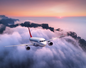 Passenger airplane is flying over clouds at sunset. Landscape with white airplane, low clouds, sea...