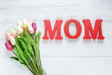 Word Mum from red letters and tender tulips on white wooden background. Mothers day decoration concept. Top view, flat lay with copy space