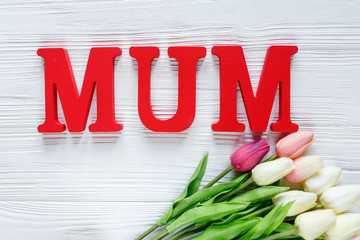 Word Mum from red letters and tender tulips on white wooden background. Mothers day decoration concept. Top view, flat lay with copy space