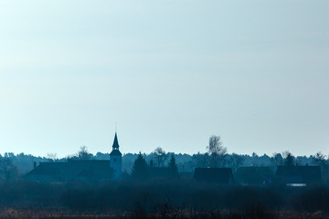 minimalistic mystical landscape in blue colors with the silhouette of the church tower in a small village in the morning mist