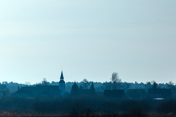 Fototapeta premium minimalistic mystical landscape in blue colors with the silhouette of the church tower in a small village in the morning mist