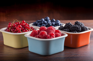 Berries fresh arrangement in colorful ceramic jars on rustic wooden table and dark background front view in studio