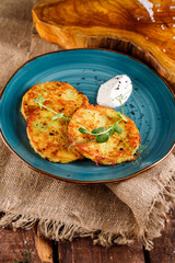 Close-up view of potato pancakes. Potato cake on a blue plate above a wooden table, with fresh parsley and sour cream.