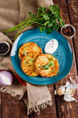 Close-up view of potato pancakes. Potato cake on a blue plate above a wooden table, with fresh parsley and sour cream.