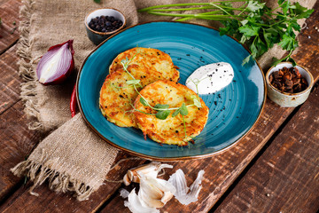 Close-up view of potato pancakes. Potato cake on a blue plate above a wooden table, with fresh parsley and sour cream.