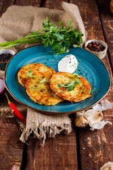 Close-up view of potato pancakes. Potato cake on a blue plate above a wooden table, with fresh parsley and sour cream.