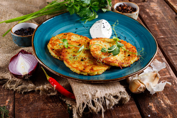 Close-up view of potato pancakes. Potato cake on a blue plate above a wooden table, with fresh parsley and sour cream.