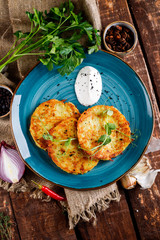 Close-up view of potato pancakes. Potato cake on a blue plate above a wooden table, with fresh parsley and sour cream.