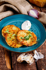 Close-up view of potato pancakes. Potato cake on a blue plate above a wooden table, with fresh parsley and sour cream.