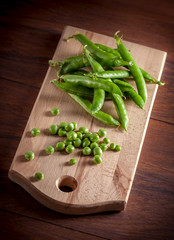 Peas on cutting board and brown wooden table arrangement on dark backgound studio shot