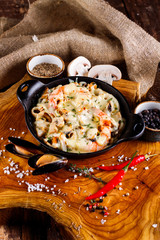 Tasty seafood in white sauce on a metal black plate.