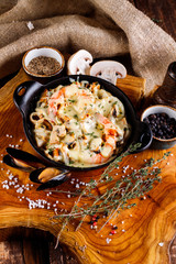 Delicious seafood in white sauce on a metal black plate, a number of products for cooking, tomatoes, champignons.