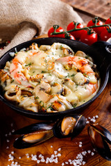 Tasty seafood in white sauce on a metal black plate.