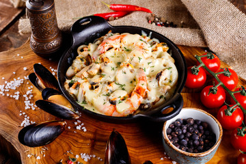 Delicious seafood in white sauce on a metal black plate, a number of products for cooking, tomatoes, champignons.