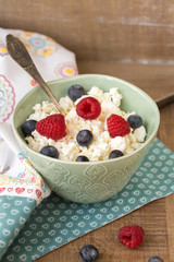 Cottage cheese with fresh raspberries and blueberries in a bowl for healthy breakfast with ripe berries over rustic wooden background.