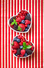 Berries arrangement in heart shaped ceramic jars on stiped red and white background studio shot. Raspberries, strawberries, blueberries, blackberies, red currant