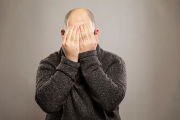 Bald man covered his face with his hands, gray background