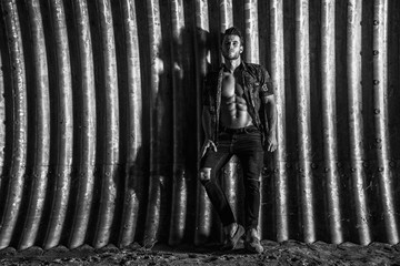 Obraz premium Muscular young man with beard on dark tunnel urban background. Fashion portrait of brutal strong muscle guy with modern trendy hairstyle. Model, fashion concept. Sexy naked torso. Black and white.