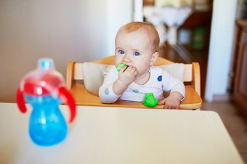 Little baby girl sitting in high chair and drinking water from sippy cup